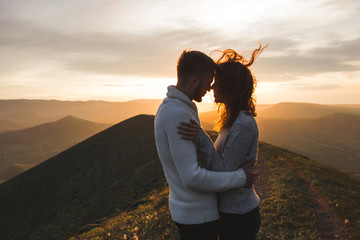 Happy couple hugging and kissing at sunset witn amazing mountain view. Warm evening sun light