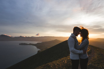 Happy couple hugging and kissing at sunset witn amazing mountain view. Warm evening sun light