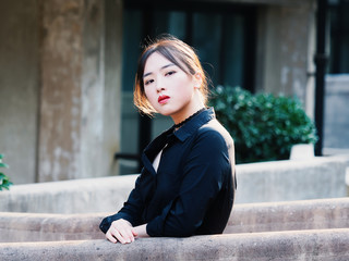 Fototapeta premium Beautiful Chinese young girl wearing black shirt looking and smiling at camera in summer city with back light and building background. Outdoor fashion portrait of glamour sexy stylish lady.