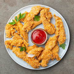 Breaded chicken strips with tomato ketchup on a white plate. Fast food on dark brown background....