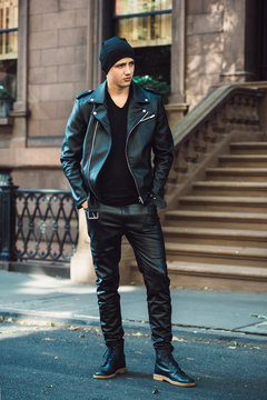 Hipster man wearing black style leather outfit with hat, pants, jacket and shoes standing on city street
