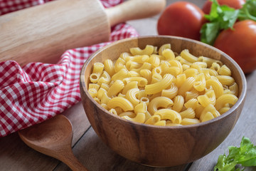Raw macaroni pasta in wooden bowl