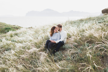 Fototapeta na wymiar Happy young loving couple sitting in feather grass meadow, laughing and hugging, casual style sweater and jeans