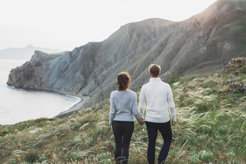 Young couple walking on nordic sea coast with mountain view in spring, casual style clothing...