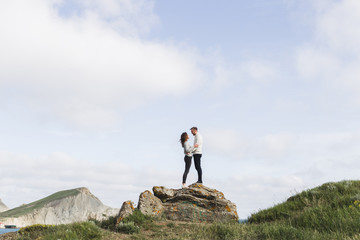 Obraz premium Young couple walking on nordic sea coast with mountain view in spring, casual style clothing sweaters and jeans