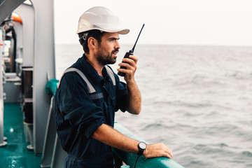 Marine Deck Officer or Chief mate on deck of vessel or ship . He holds VHF walkie-talkie radio in...