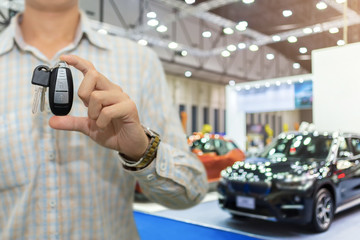 Salesman or dealer offering car keys to new owner in showroom, buy or rent concept.