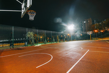 Illuminated basketball playground with red pavement, modern new basketball net and lens flares on...