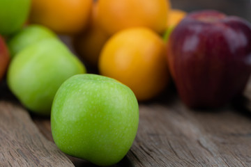 Green apple is placed on a wooden floor with a blurred background as well as other fruits.