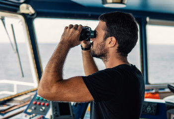 Navigational officer lookout on navigation watch looking through binoculars. Marine industry....