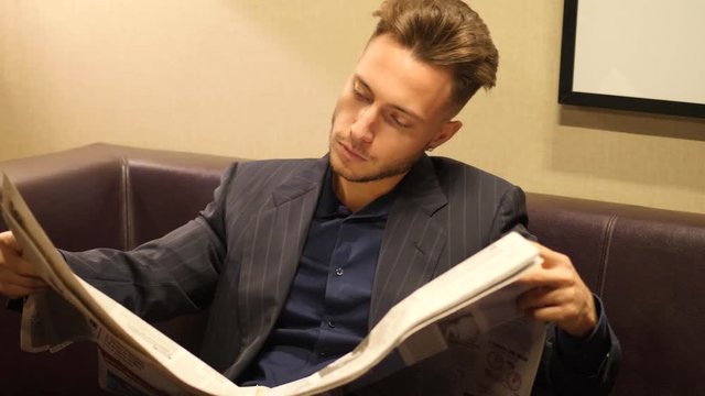 Handsome young business man at home reading newspaper, sitting on couch