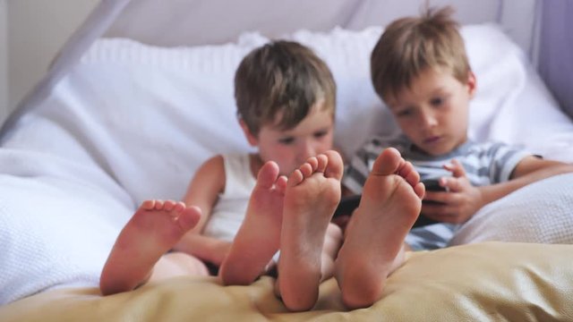 Two boys holding smartphone, tablet sitting on chair, focus on childrens feet.