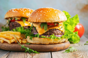 Two fresh homemade burgers with fried potatoes on a wooden table