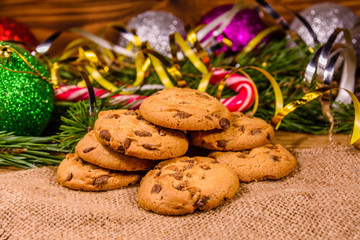 Pile of the chocolate chip cookies on sackcloth in front of christmas decorations