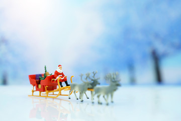 Miniature people: Santa Claus sitting Reindeer Sleigh with greeting or postal card and christmas tree. Christmas and Happy New Year concept.