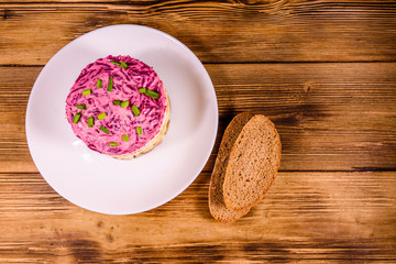 White plate with russian traditional new year salad herring under fur coat and rye bread on wooden table. Top view