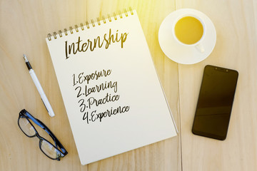 Top view of sunglasses,pen,mobile phone, a cup of coffee,and notebook written with Internship benefits, experience,learning,exposure,practice. Business and education concept.