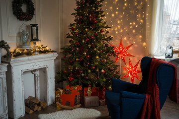 Christmas and new year's interior in the house. Cozy Christmas in the house, Christmas decorations: red glowing stars, blue chair, red plaid, artificial Christmas tree with lights garland