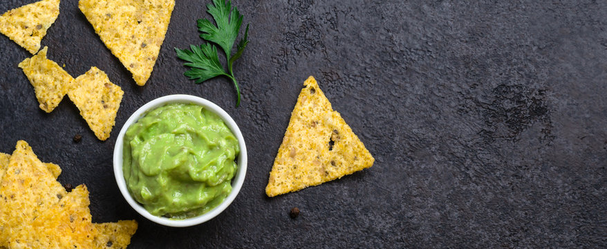 Traditional Mexican food guacamole and corn chips on black background. Banner format