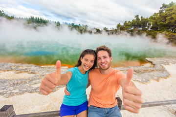 New Zealand happy tourist couple doing thumbs up at famous attraction travel destination. Champagne...