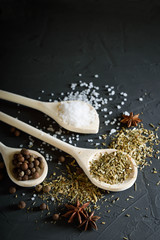  Wooden spoon with Italian seasoning-dried oregano with thyme vegetables.Oregano in a wooden spoon on a rocky concrete dark black background with a place for text.Top view.salt crystals pepper