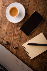  Laptop (notebook) mobile phone (smartphone) and notepad with pen on old wooden table. Work place modern.Cup of coffee