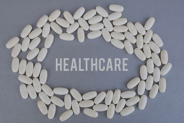 Circle of white medicine tablets or pills on silver color background with word healthcare in middle.  Pharmacy concept.
