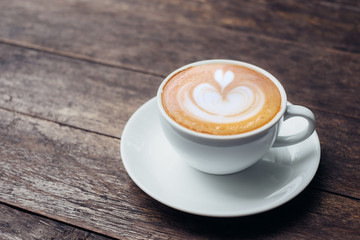 Close up white coffee cup with heart shape latte art on grunge wood table at cafe.