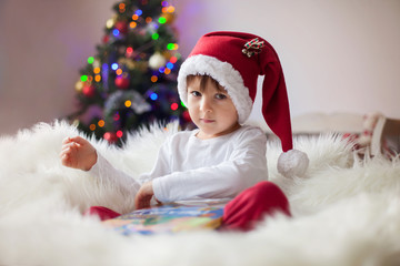 Cute adorable boy reading a book in front of the christmas tree
