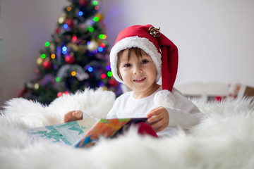 Cute adorable boy reading a book in front of the christmas tree