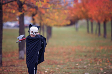 Children having fun with halloween carved pumpkin in a park, wearing scary costumes