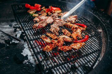 Grilled meat and vegetables in barbecue with flames and coals.