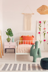 Macrame on the wall of cozy girl's bedroom with flower board and single metal bed with pillows, real photo with copy space
