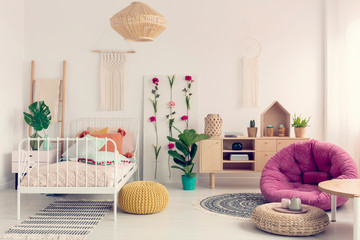 Stylish pink settee in the middle of elegant boho bedroom with macrame on the wall, flower board...