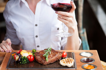 Woman eating steak and drinking a wine