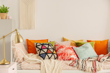 Patterned and colorful pillows on comfortable white bed in stylish bedroom interior with golden...