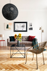 Real photo of sunflowers in an eclectic living room interior with herringbone parquet, sofa and...