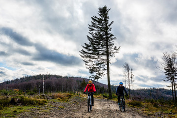 Fototapeta premium Cycling woman and man at Beskidy mountains autumn forest landscape. Couple riding MTB enduro track. Outdoor sport activity.