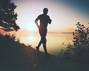 Man runs on pavement in lake bay. Regular morning training - obrazy, fototapety, plakaty