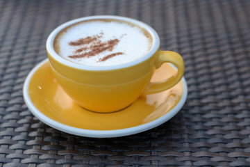 Close up of hot cappuccino coffee in a yellow cup on black table background in cafe.