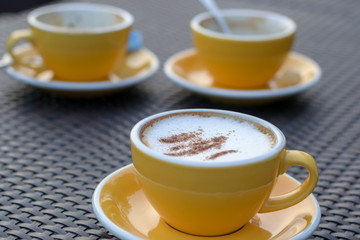 cappuccino coffee in yellow cup on table at cafe.