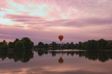 Naklejka premium Picturesque view of medieval Telc during magic sunrise. One hot air balloon flies over the houses and reflected on smooth lake water. Summer landscape. Telc, Southern Moravia, Czech Republic