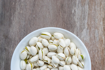 pistachios in white ceramic bowl on wooden background with copyspace 