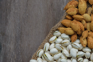 Almonds and pistachios on natural sack with the old wood table background.