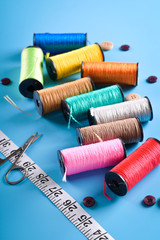 Sewing kit: scissors, measuring tape, thimbles, threads and buttons. Composition with threads and sewing accessories on blue background