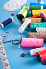 Sewing kit: scissors, measuring tape, thimbles, threads and buttons. Composition with threads and sewing accessories on blue background