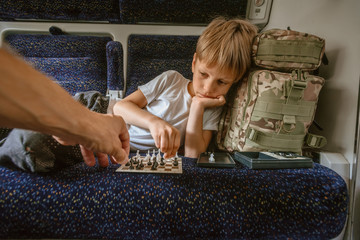 Young smart boy playing chess with parent in train