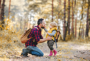 A toddler boy giving an apple to his father in an autumn forest.