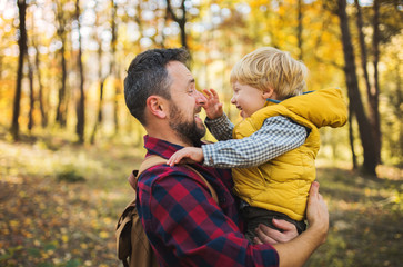 A mature father holding a toddler son in an autumn forest, having fun.
