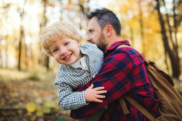 Fototapeta premium A mature father holding a toddler son in an autumn forest, having fun.